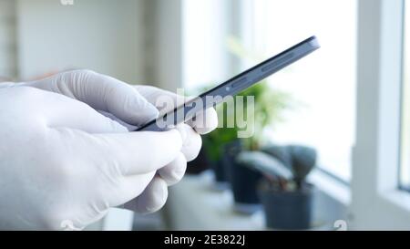 Image with Doctor Hands Wearing Protective Gloves Browsing Internet Connection and Sending an Email Using a Smartphone Stock Photo