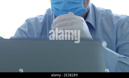 Doctor in a Hospital Office with a Face Mask and Protective Gloves Using a Laptop Stock Photo