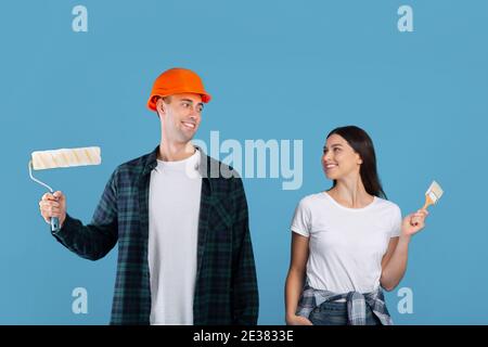 Happy Young Couple With Painting Tools In Hands Posing Over Blue Background Stock Photo