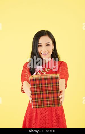 Cheerful pretty young Asian woman outstretching hands with big present for Chinese New Year celebration Stock Photo