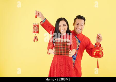 Smiling woman with Lunar New Year gift and her boyfriend showing wall decorations with best wishes inscription Stock Photo