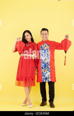 Happy young man and woman in traditional costumes for Lunar New Year celebration showing paper lanterns Stock Photo
