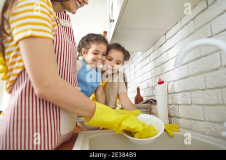 Two girls learning to do domestic chores and watching mother wash the dishes after lunch Stock Photo