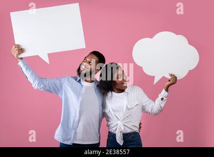 Portrait of young African American couple holding empty speech bubbles with space for your design on pink background Stock Photo