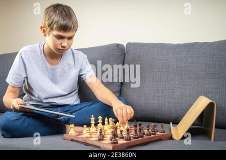 Teenage boy learning to play chess online with tablet computer