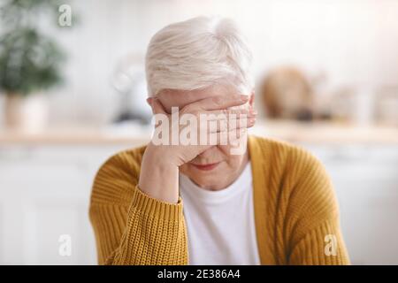 Senior woman suffering from migraine, kitchen interior Stock Photo
