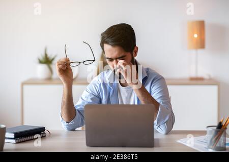 Eye Strain. Tired Arab Freelancer Guy Feeling Exhausted After Working On Laptop Stock Photo