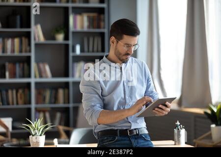 Focused young businessman in glasses using digital computer tablet. Stock Photo