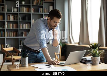 Thoughtful young businessman working on computer standing at table. Stock Photo
