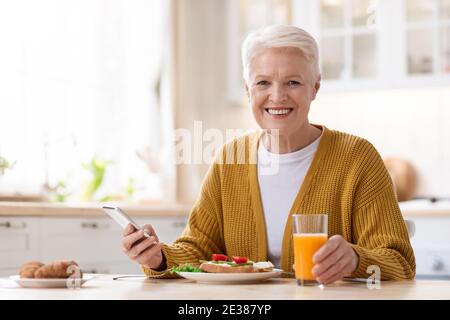 Smiling old lady using mobile phone while having lunch Stock Photo