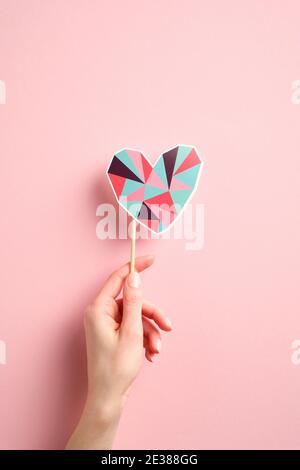 Woman's hand holding heart shaped decoration over pink background. Minimal style. Happy Valentines day concept. Stock Photo