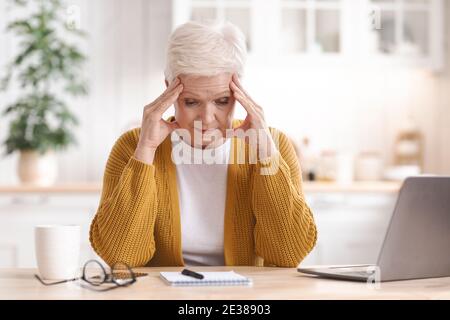 Exhautsed mature woman freelancer working from home, using laptop Stock Photo