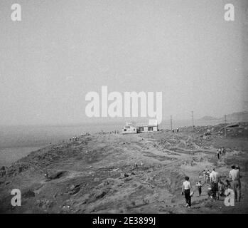 1950s, historical, visitors on the rocky landscape on the far south-west corner of England, Lands End, Cornwall. The famous tea rooms and souvenir cottage, the 'First & Last House in England' can be seen in the distance. Stock Photo