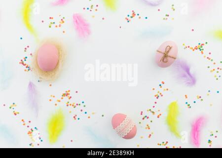Ester frame composition with colorful eggs, feathers and confetti on white background. Flat lay, top view Stock Photo