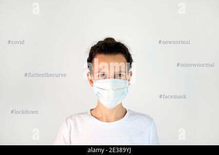 Woman wearing a face mask surrounded by Covid related social media hashtags. Stay home, face mask, flatten the curve, new normal, no new normal, lock Stock Photo