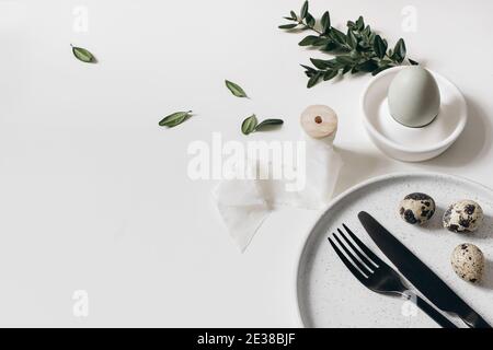 Festive Easter breakfast table setting. Spring still life with black cutlery, ceramic plate and green buxus leaves isolated on white background Stock Photo