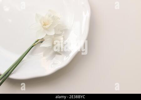 Styled stock photo. Spring, Easter feminine desktop scene with white narcissus, daffodils flowers on porcelain plate. Beige table background. Floral Stock Photo