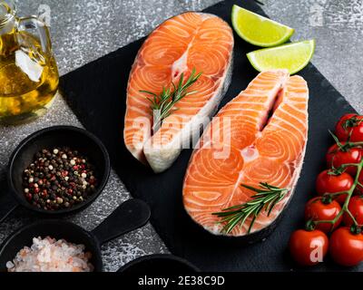 two raw steak fish trout, salmon and spices on black stone surface, dark Stock Photo