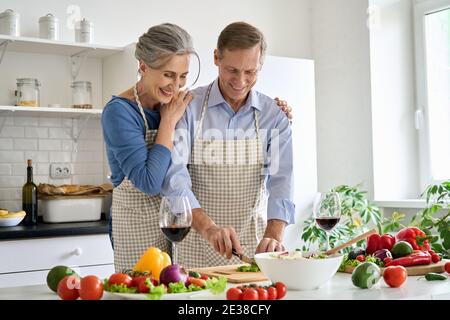 Happy old senior couple preparing vegetable salad cooking in kitchen at home. Stock Photo