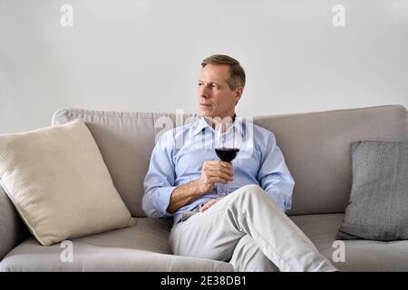 Relaxed old retired single man drinking wine relaxing on sofa at home. Stock Photo