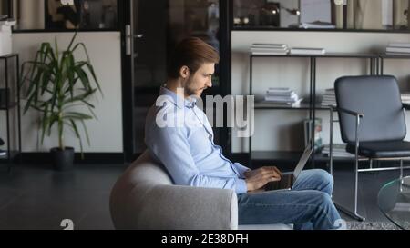 Confident businessman using laptop, sitting in armchair in modern office Stock Photo