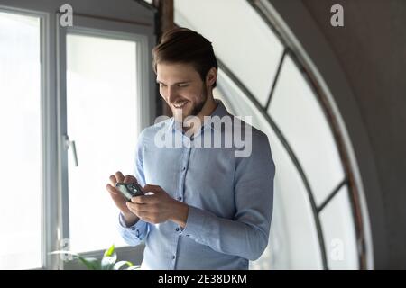 Close up smiling businessman using smartphone, standing in office Stock Photo