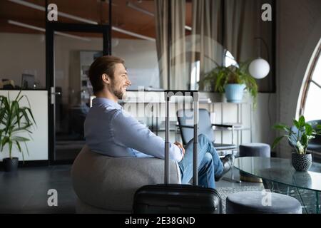 Smiling confident businessman sitting in armchair, arrived after airport Stock Photo