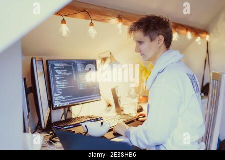 A man sitting at a desk working from home on his computer. IT specialist programmer writing code on his pc and laptop. Developer remote home office Stock Photo