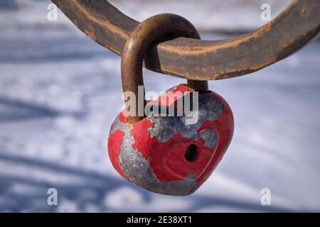 Red heart-shaped padlock on the cast iron fence of the bridge close-up. Stock Photo