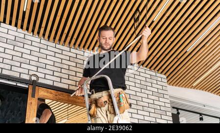 Installation of wooden plank ceiling and electrical wiring in a new apartment. Service for replacing LED lamps and repairing electrical wiring. Electr Stock Photo