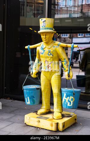 Hamburg, Germany - August 23, 2019: Yellow human figure with top hat and holding two cubes on a scale on a street in Hamburg, Germany Stock Photo