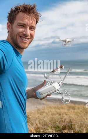 Person flying a drone on beach outdoors gaming young man pilot controlling drong with controller and smart phone taking selfie on travel vacation Stock Photo