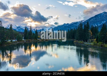 Bow River riverbank in autumn season sunset time. Beautiful fiery clouds reflect on water surface like a mirror. Beautiful nature scenery in Banff Stock Photo