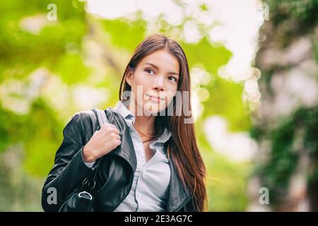 Asian woman young beautiful adult walking commute going to work with purse and black leather jacket in spring outdoor city street lifestyle Stock Photo