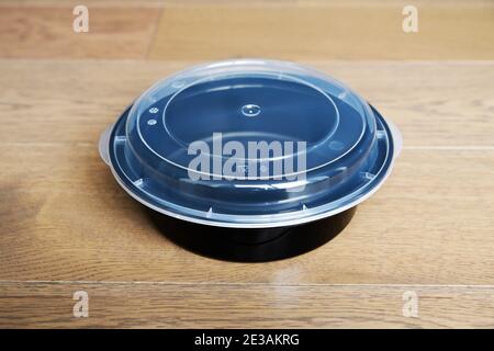 Black plastic bowl with clear lid on wooden floor for food. Stock Photo