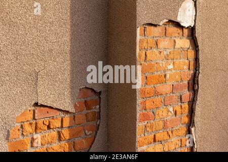 Shabby chic texture background of an old red clay brick wall, exposed underneath a peeling and deteriorating sandy brown color stucco wall Stock Photo