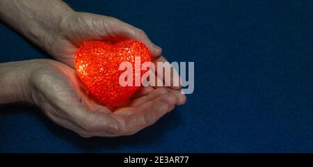 Red flaming heart in strong male hands on a blue background. Valentine's day concept. The theme of love and care for the health of your heart. Banner. Stock Photo
