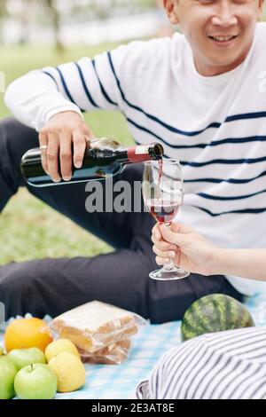 Cropped image of man pouring red wine in glass for his girlfriend at date Stock Photo