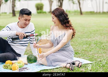 Happy young Asian couple enjoying good wine when having date in park on Valentines day Stock Photo