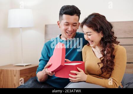 Young man looking at reaction of his girlfriend opening present for Valentines day Stock Photo