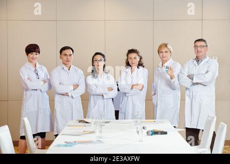International group of scientists in labcoats standing in conference room after discussing advantages of new coronavirus vaccine Stock Photo