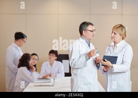 Mature researchers with digital tablet discussing advantages of new vaccine at meeting Stock Photo
