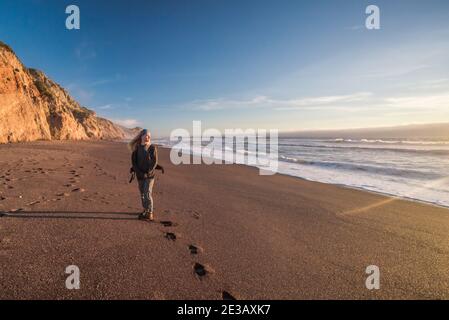 A lone woman stands on a empty beach in Point Reyes national seashore, California looking out at the Pacific ocean. Stock Photo