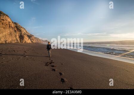 A female hiker walks down a California beach in the evening, a portion of the Alamere falls trail in Point Reyes National seashore. Stock Photo