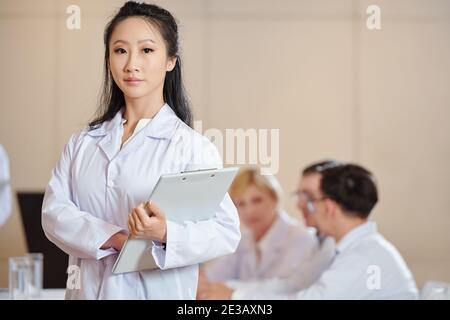 Serious young female Chinese scientist with clipboard standing in conference room and looking at camera Stock Photo
