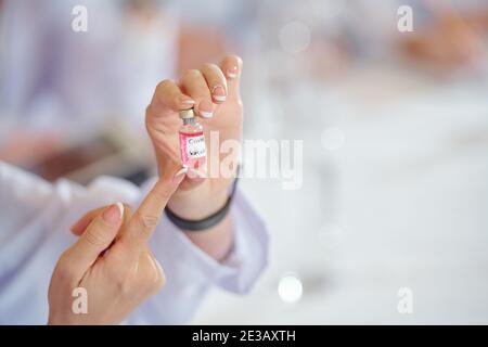 Hands of young female researcher holding vial with new vaccine her team developed and talking about its advantages Stock Photo