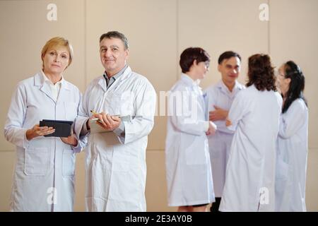 Mature scientists with tablet computers standing in hall after having conference with younger colleagues Stock Photo