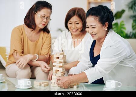 Group of cheerful Asian senior women playing strategy game with blocks of wood and drinking tea Stock Photo