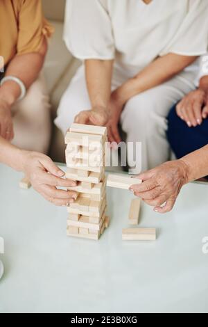 Close-up image of aged women taking wooden blocks out of tower when playing strategy game at home Stock Photo