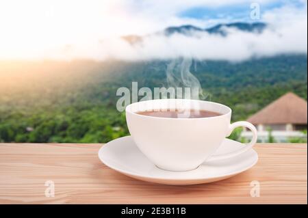 tea cup on mountain background. cup with organic tea leaf on the wooden table and tea plantations. Cup with tea on table over mountains landscape with Stock Photo